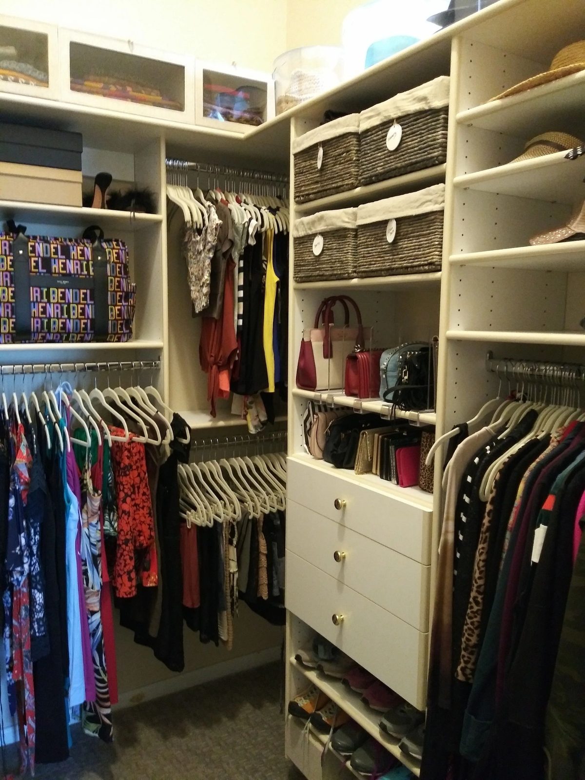 Organized walk-in closet with clothes, handbags and hats sorted on white shelving